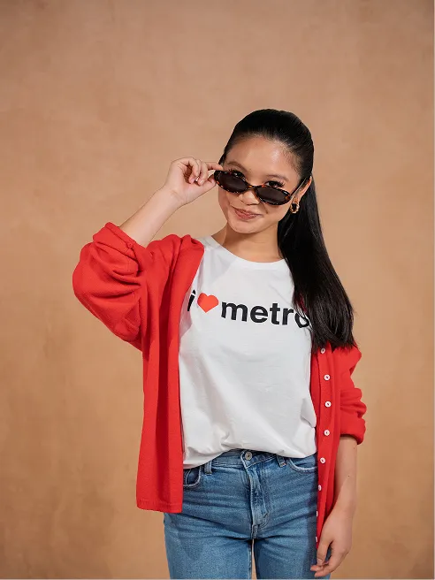 A model in a white tee with a red heart and 'metro', lowering her sunglasses."